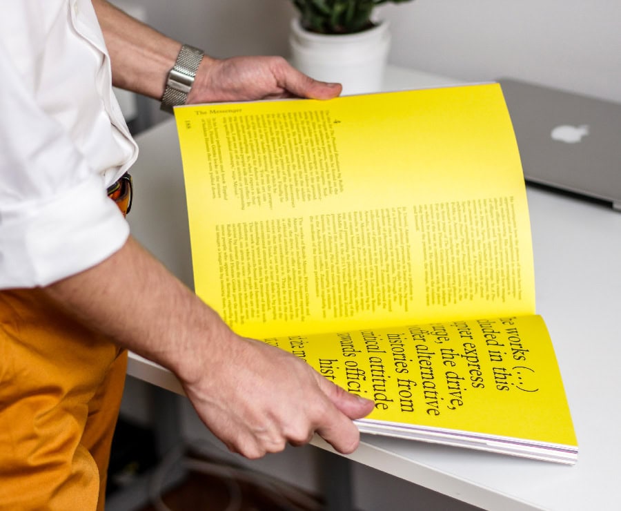 Personne tenant un livret jaune avec texte, vue de côté.