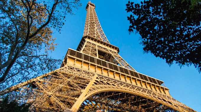 Eiffel Tower vue du sol avec ciel bleu et arbres en arrière-plan.